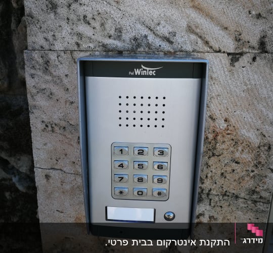 אינטרקום מתכת עם לוח מקשים על קיר אבן